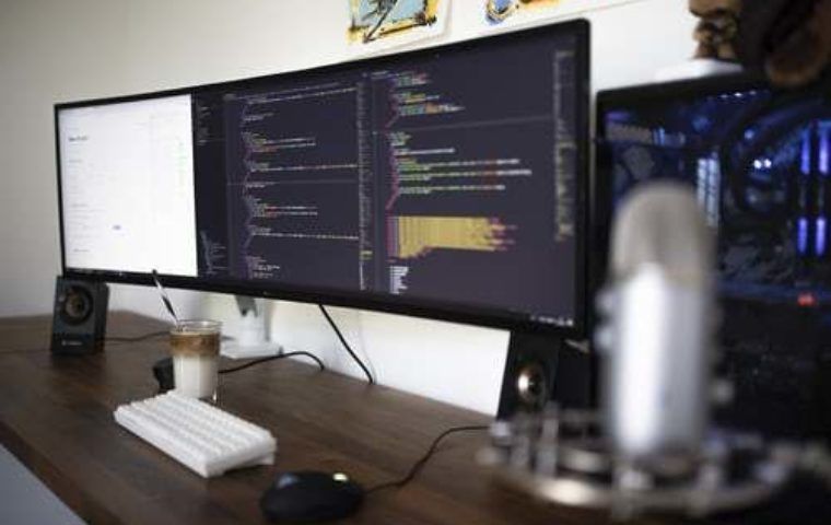 Image of three computer screens with coding on two of the screens