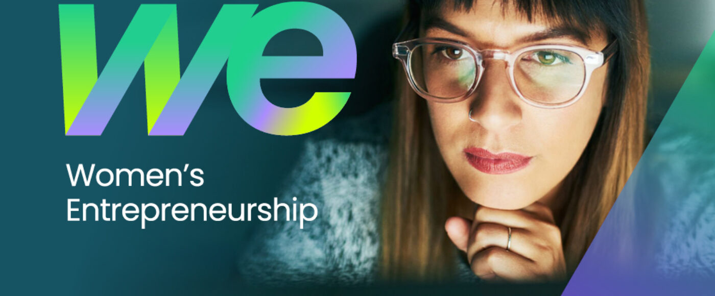 Homepage banner image for the Women’s Entrepreneurship (WE) campaign. Shows the WE logo in green and purple alongside a woman working at a computer