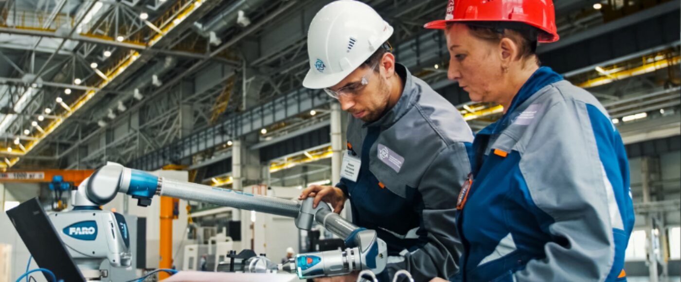 Two workers using manufacturing equipment in an industrial production facility.