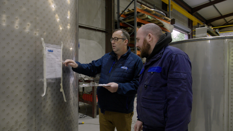 Pádraig Lynch pointing to a piece of paper on a milk tank in the Liscarroll factory